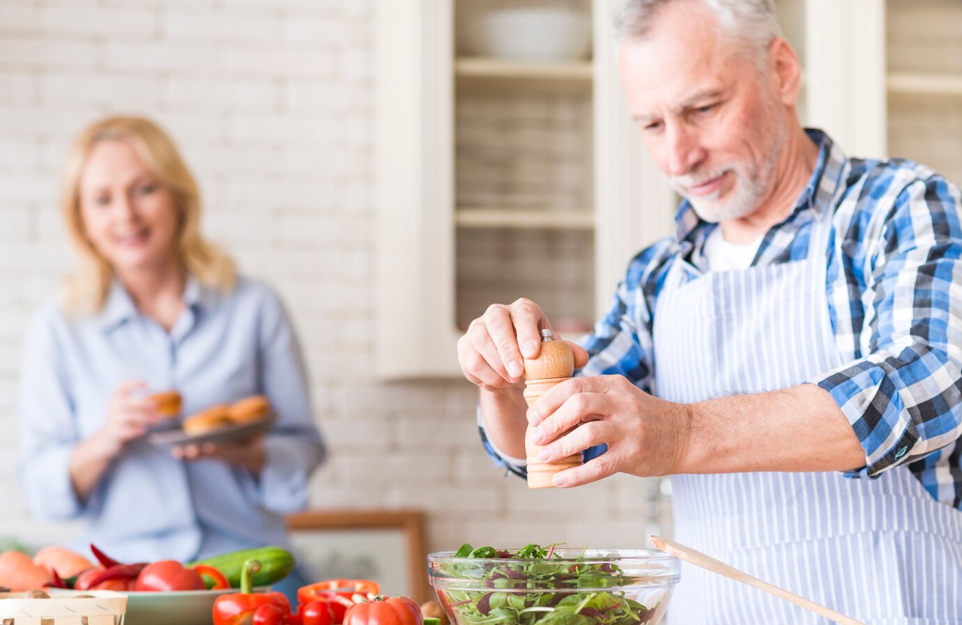 senior-man-grinding-pepper-salad-her-wife-enjoying-muffins-background-kitchen_23-2148128117